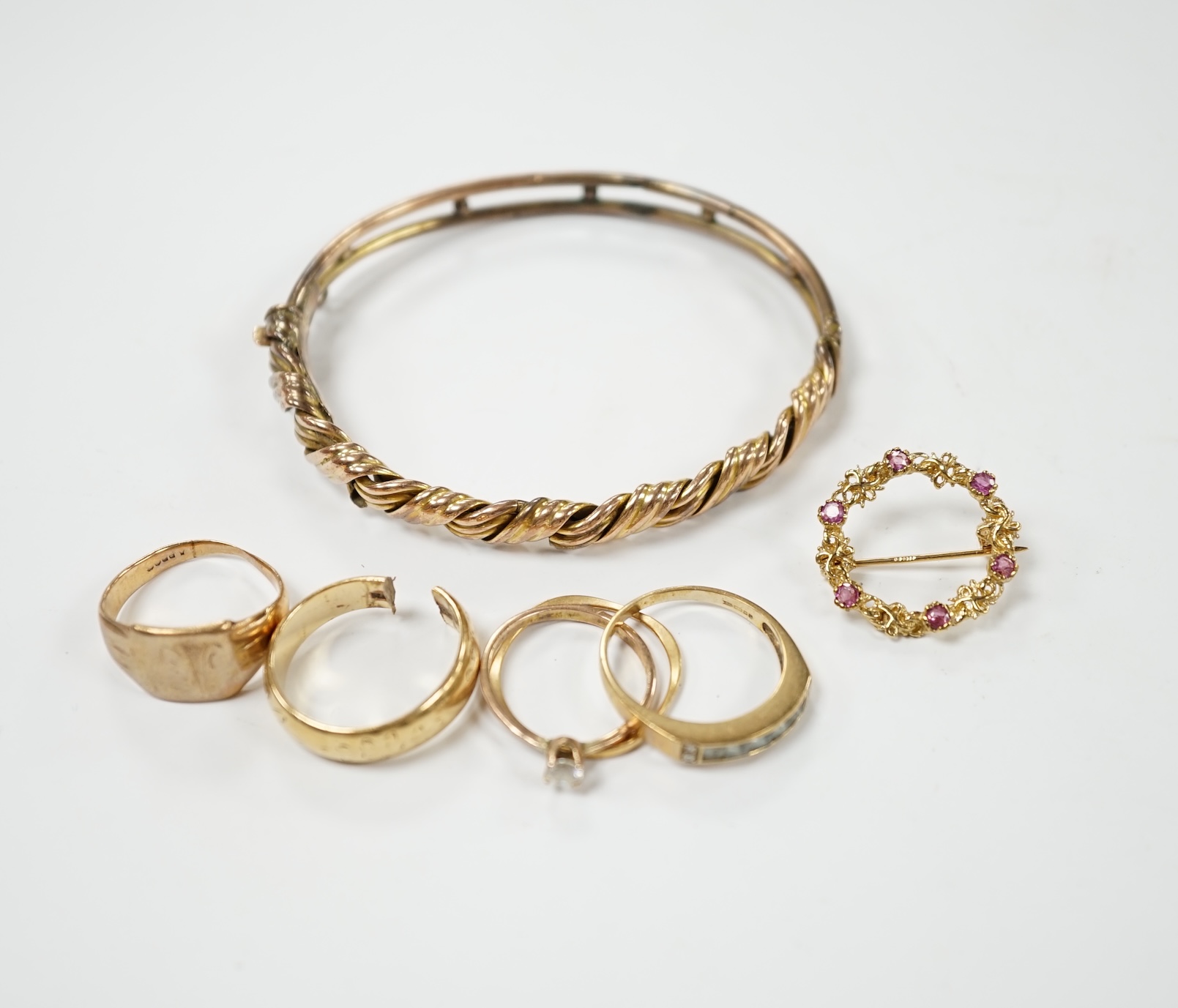 An early 20th century 9ct hinged bangle, three assorted 9ct gold rings and a modern 9ct gold and gem set brooch and two other yellow metal rings, gross weight 23.2 grams. Condition - poor